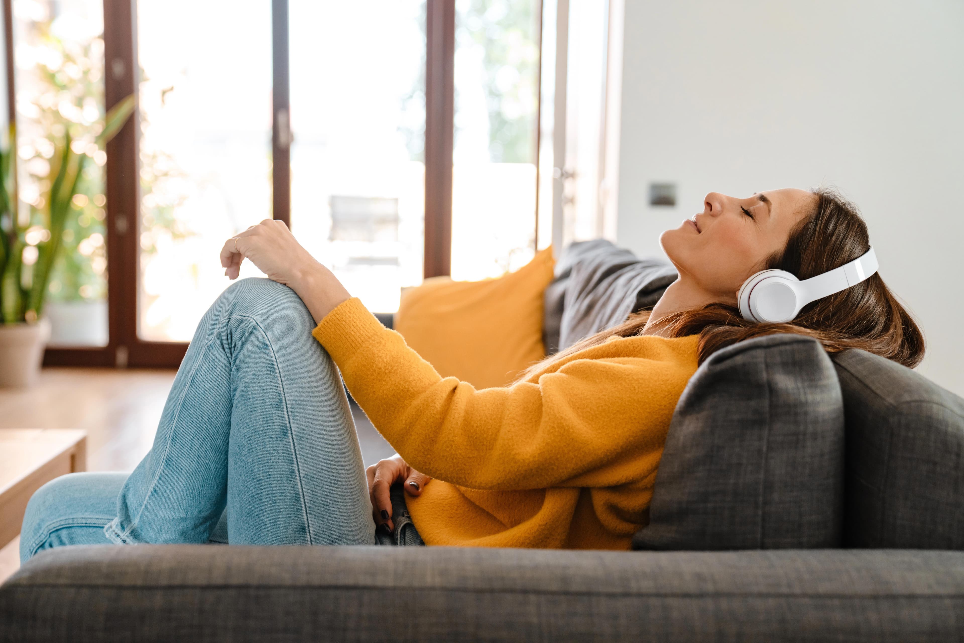 A young patient is enjoying music through headphones on her couch.