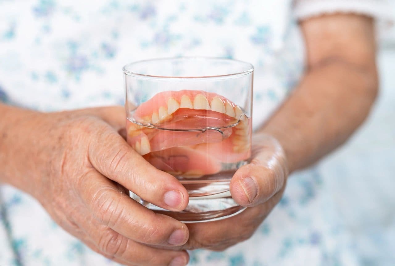 Photo of a patient holding a glass with soaking dentures inside