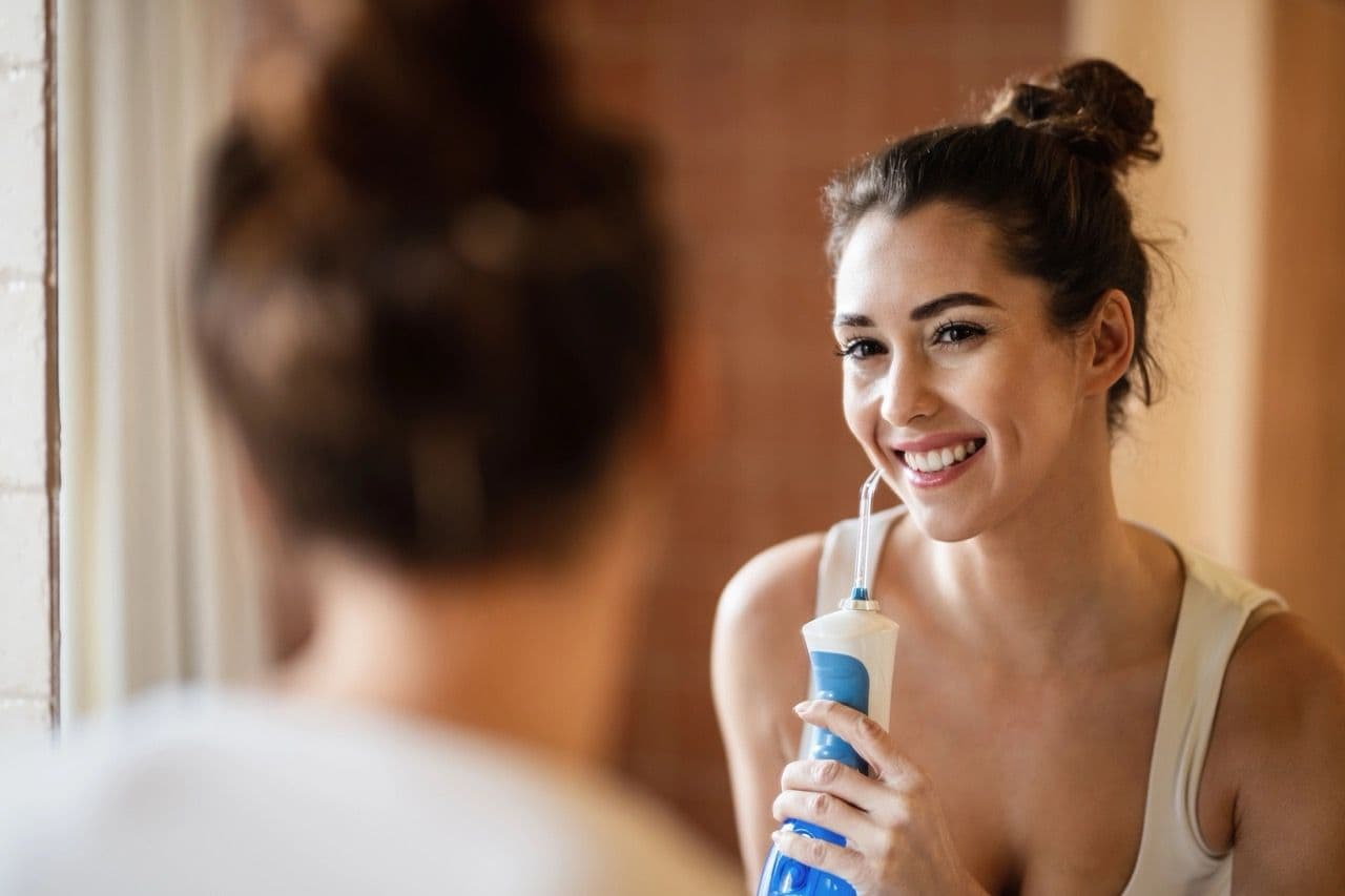 Photo of a woman looking in the mirror while using a water flosser