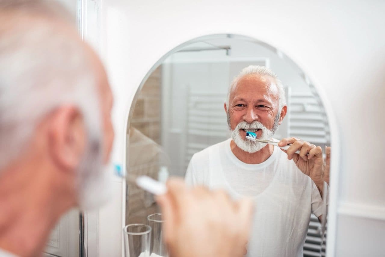 Photo of a man looking in the mirror while brushing his teeth