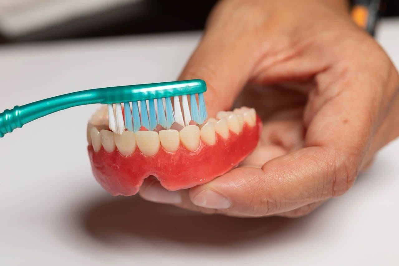 A photo of someone using a toothbrush to clean dentures