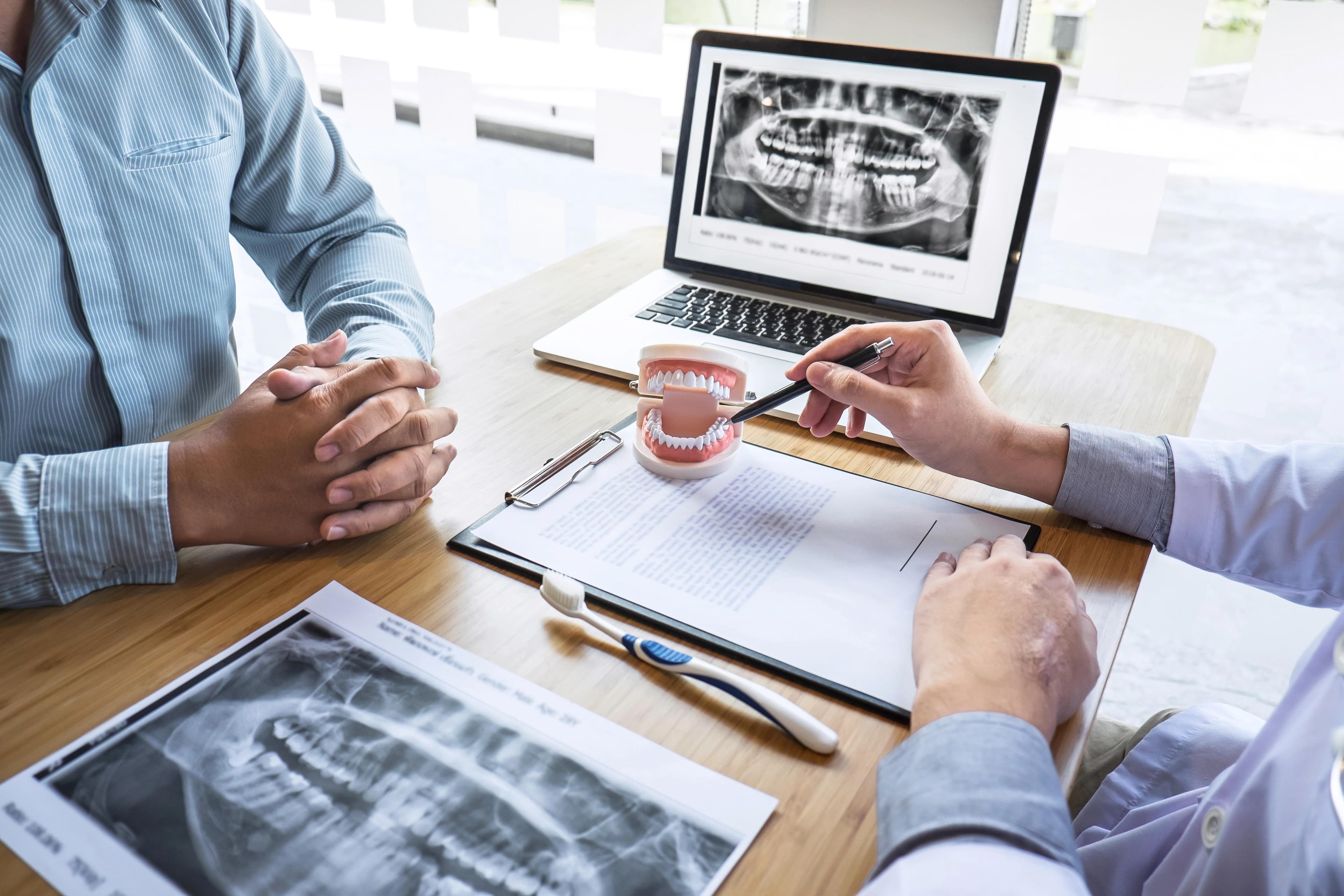 A dentist is showing a patient a set of dentures on his desk.