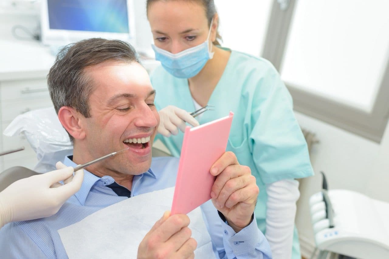 A happy patient examining their teeth in a handheld mirror