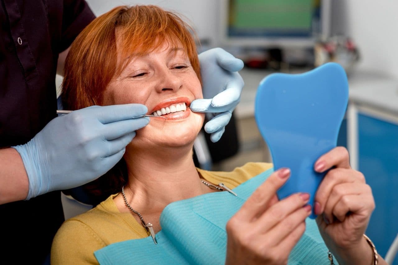 Photo of a patient examining her teeth in a handheld mirror