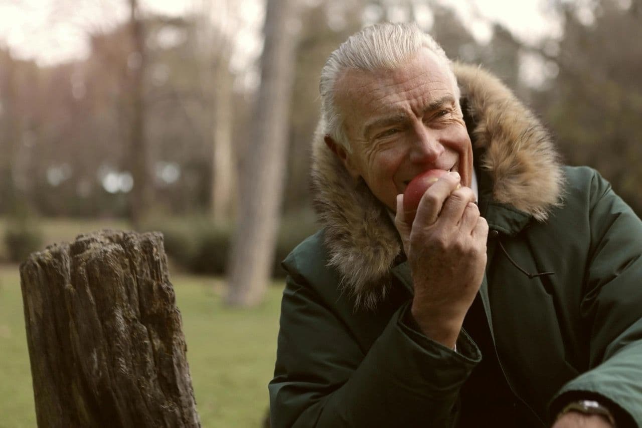 An gray-haired man eating an apple