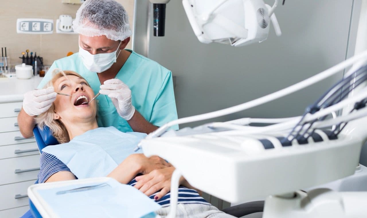 Photo of a patient lying back with a dentist using tools in her mouth